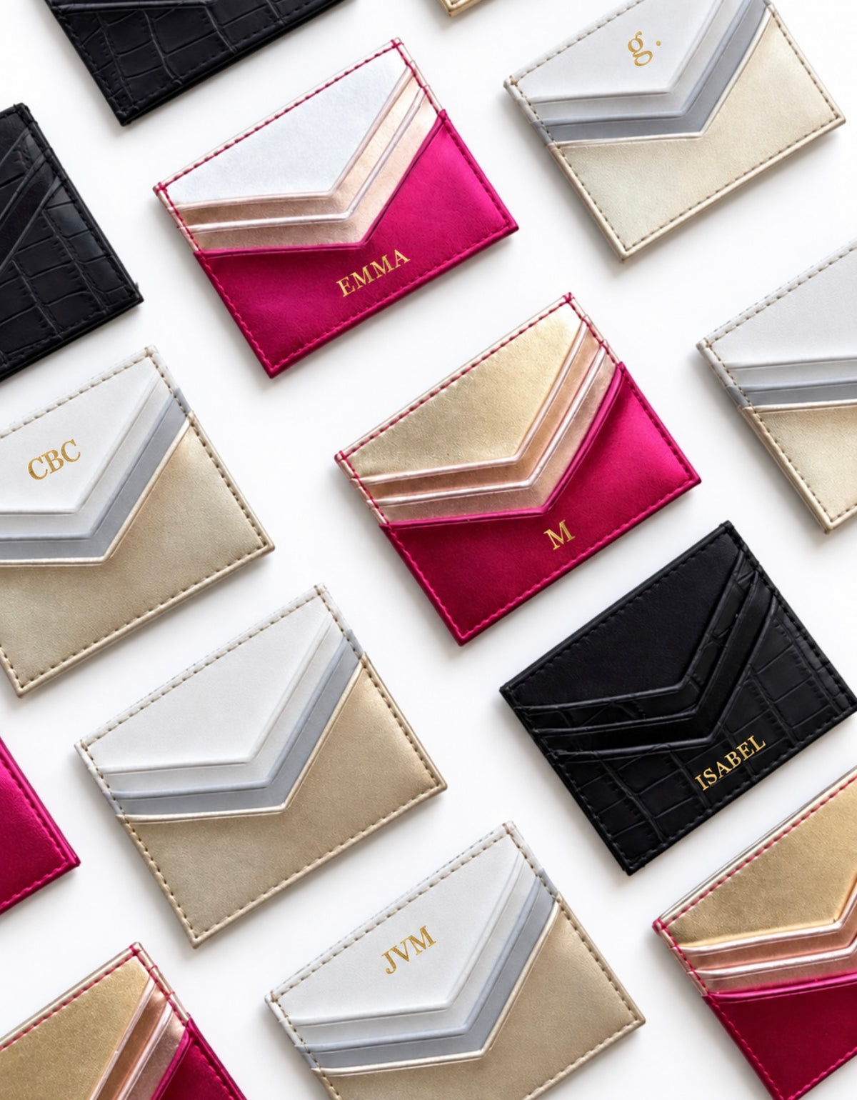 A styled flat-lay of multiple personalized chevron card holders on a white background. The holders feature metallic gold, silver, and vibrant magenta pink panels, with some in textured black leather.
